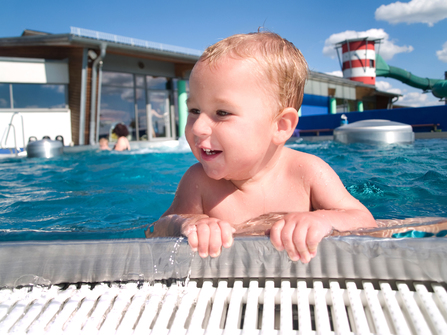 glückliches Baby schwimmt im Freibad im blauen Wasser
